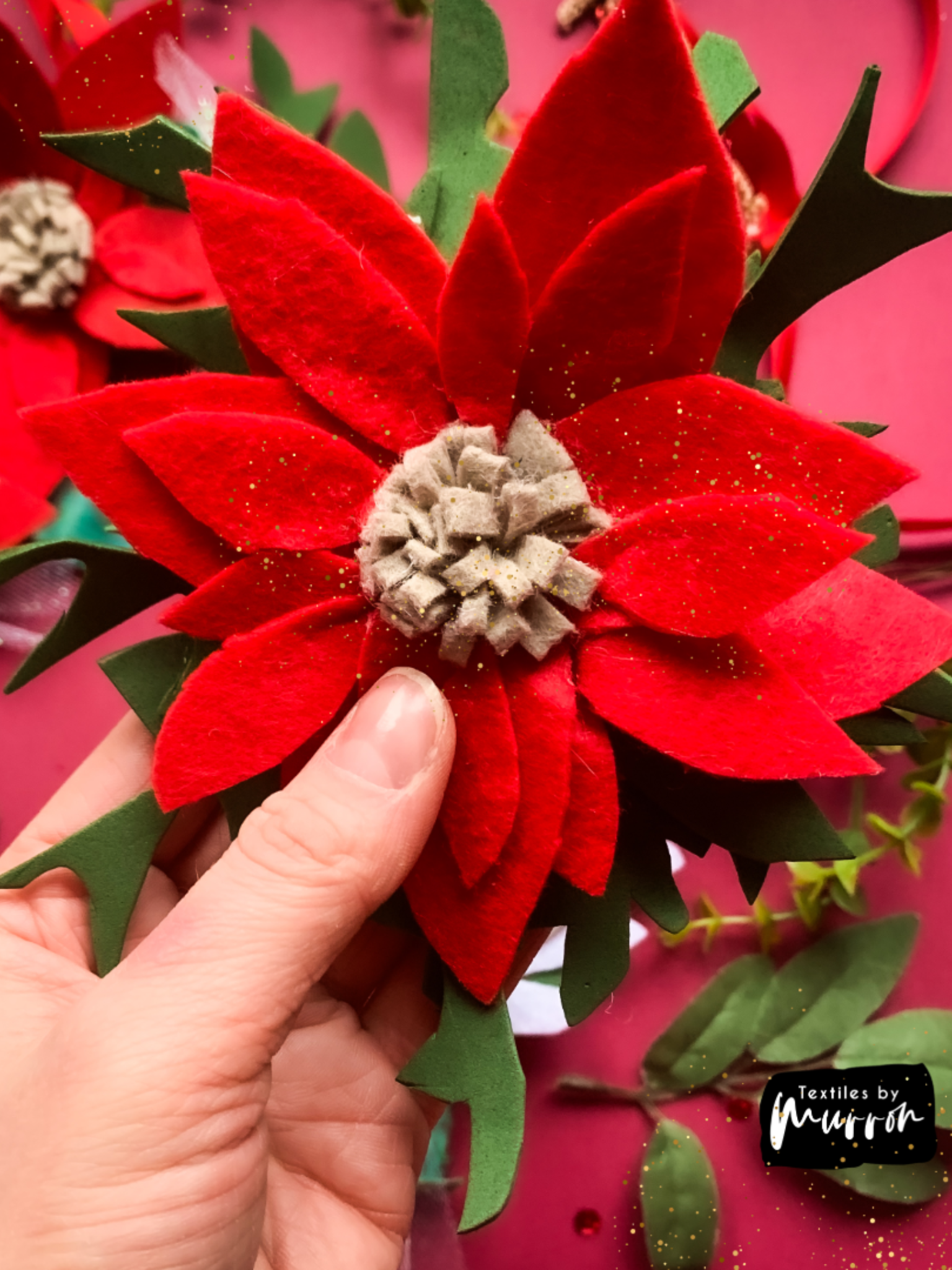 Red and green textile wreath close up made in the festive workshop on a red table